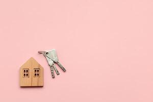 houten huis model- met sleutels Aan roze achtergrond. hypotheek concept. foto