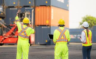 groep van arbeiders in de importeren en exporteren industrie gebruik walkie talkies naar communiceren met chauffeurs van bereiken stapelaar containers in een leeg houder magazijn. foto