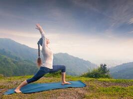 vrouw aan het doen yoga asana virabhadrasana 1 krijger houding buitenshuis foto