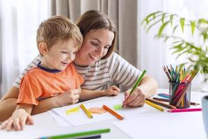 moeder helpt kind met artwork gebruik makend van gekleurde potloden foto