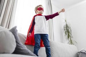 jong jongen in superheld kostuum spelen Bij huis. foto