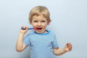 weinig blond jongen poetsen tanden met tandenborstel Aan blauw achtergrond foto