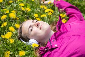 mooi jong vrouw in hoofdtelefoons luistert naar muziek- aan het liegen Aan de gras foto