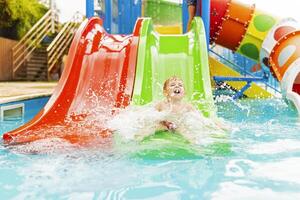 weinig jongen spelen Aan water glijbaan in buitenshuis zwembad Aan een heet zomer dag foto