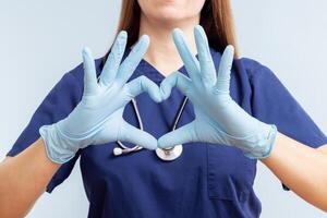 dokter vrouw in handschoenen aan het doen hart symbool vorm met handen Aan blauw achtergrond foto