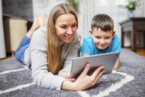 gelukkig liefhebbend familie. jong moeder en haar zoon gebruik makend van tablet aan het liegen Aan tapijt foto