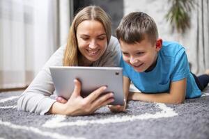 gelukkig liefhebbend familie. jong moeder en haar zoon gebruik makend van tablet aan het liegen Aan tapijt foto