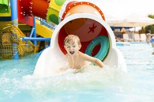 weinig jongen spelen Aan water glijbaan in buitenshuis zwembad Aan een heet zomer dag foto