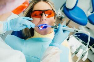 een jong mooi meisje in tandheelkundig bril behandelt haar tanden Bij de tandarts met ultraviolet licht. vulling van tanden foto