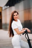mooi meisje in wit elegant kleren Aan een elektrisch scooter in de stad foto