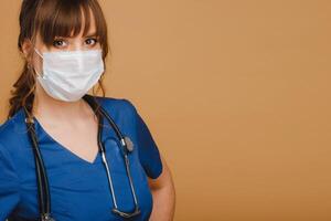 een meisje dokter staat in een medisch masker, geïsoleerd Aan een bruin achtergrond foto