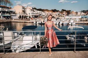 jong model- meisje in een mooi jurk met een boeket van bloemen Aan de strand in Frankrijk. meisje met bloemen in voorjaar provence Aan de Frans riviera foto