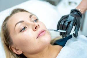 detailopname van vrouw gezicht en hand- in chirurgisch handschoen Holding injectiespuit in de buurt haar lippen, klaar naar te ontvangen schoonheid behandeling. injectie cosmetologie, lippen vergroting en correctie concept. foto