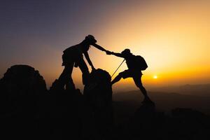 silhouet van mensen helpen elk andere wandeltocht omhoog een berg Bij zonsopkomst. geven een helpen hand, en actief fit levensstijl concept. helpen en succes concept, leiderschap concept, teamwerk. foto