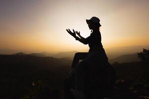 silhouet van een Dames is bidden naar god Aan de berg. bidden handen met geloof in religie en geloof in god Aan zegen achtergrond. macht van hoop of liefde en toewijding. foto