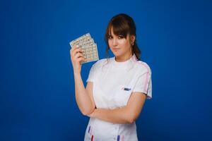 de concept van Gezondheid zorg. een jong brunette dokter in een wit jas Aan een blauw achtergrond shows borden met capsules naar nemen. foto