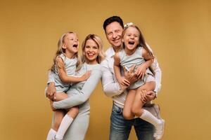 gelukkig ouders houden hun kinderen in hun armen en glimlach Aan een geel achtergrond. een emotioneel familie van vier foto