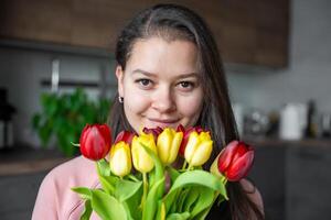 portret van mooi jong vrouw met een boeket van rood en geel tulpen Bij huis. Gefeliciteerd en een geschenk Aan Internationale vrouwen dag of moeder dag foto