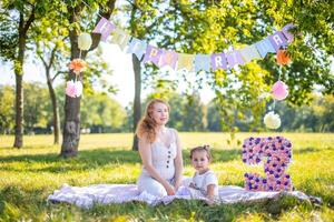 vrolijk moeder en dochter hebben pret Aan kind verjaardag Aan deken met papier decoraties in de park foto