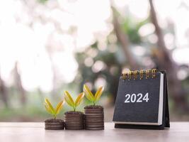 2024 bureau kalender, planten groeit omhoog Aan stack van munten. de concept van besparing geld, financieel, investering en bedrijf groeit in jaar 2024. foto