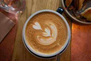 latte kunst en koffie cups met kaneel Aan de tafel, vergezeld door schotel, lepel, en suiker een verrukkelijk ochtend- drank tafereel Bij de cafe foto