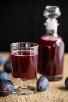 Pruim rood wijn in een glas en een karaf tegen de achtergrond van rijp groot pruimen foto