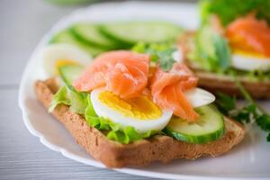 gebakken geroosterd brood met sla, ei, komkommers en rood vis in een bord. foto