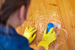 vrouw in rubber handschoenen is gebruik makend van verdieping borstel naar schoonmaak verdieping foto