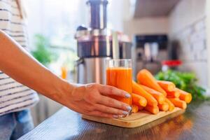 vrouw Holding glas van wortel sap met vers wortels Aan keuken teller foto