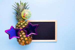 ananas in zonnebril met leeg schoolbord voor uw tekst Aan blauw achtergrond foto