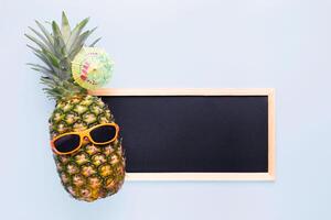 ananas in zonnebril met leeg schoolbord voor uw tekst Aan blauw achtergrond foto
