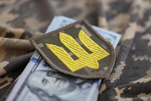 oekraïens leger symbool en bundel van dollar rekeningen Aan leger uniform. betalingen naar soldaten van de oekraïens leger van Verenigde staten, salarissen naar de leger. oorlog ondersteuning foto