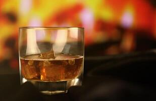 whisky of whisky of bourbon met ijs Aan houten oppervlakte Aan haard achtergrond. luxe de elite alcohol in breed glas. laag sleutel tafereel foto