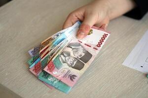 vrouw accountant hand- geven bundel van veel Indonesisch roepia geld rekeningen van nieuw serie foto