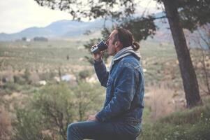 ontspannen jong Mens drinken heet thee of koffie van een thermosfles mok in de vroeg voorjaar Woud. foto