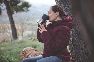 gelukkig ontspannen jong vrouw drinken heet thee van een thermosfles mok in de vroeg voorjaar Woud foto