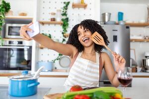 portret van glimlachen jong Afrikaanse Amerikaans vrouw nemen selfie met smartphone terwijl Koken in keuken Bij huis foto
