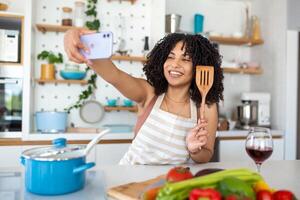 portret van glimlachen jong Afrikaanse Amerikaans vrouw nemen selfie met smartphone terwijl Koken in keuken Bij huis foto