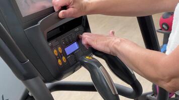 een elliptisch cross trainer is geprogrammeerd voor cardio opleiding door een vrouw hand. handen van een ouderen vrouw Aan de oefening machine. foto