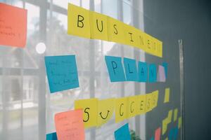 jong creatief team professioneel gebruik makend van post het aantekeningen in glas muur naar schrijven strategie bedrijf plan naar ontwikkeling toenemen naar succes. foto