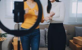 Aziatisch vrouw vrienden paar praten naar camera naar verkopen de kleren Bij huis. jong aantrekkelijk bedrijf mensen vrouw leven streaming en tonen kleding naar klant in online kleinhandel naar verkoop Bij kantoor op te slaan foto