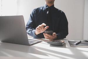 kant visie schot van een man's handen gebruik makend van slim telefoon in interieur, achterzijde visie van bedrijf Mens handen bezig gebruik makend van cel telefoon Bij kantoor bureau, jong mannetje leerling typen Aan telefoon zittend Bij houten tafel, gloed foto