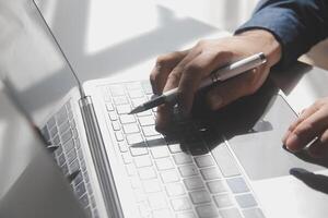 bijgesneden beeld van een jong Mens werken Aan zijn laptop in een koffie winkel, achterzijde visie van bedrijf Mens handen bezig gebruik makend van laptop Bij kantoor bureau, jong mannetje leerling typen Aan computer zittend Bij houten tafel foto