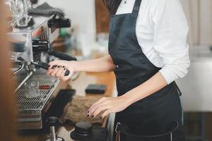 een geschoold barista in een zwart schort vakkundig opereert een espresso machine, scherpstellen Aan bouwen de perfect kop van koffie. foto