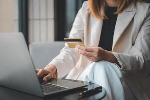 een professioneel vrouw in een modern instelling vol vertrouwen maakt een online aankoop gebruik makend van een credit kaart en een laptop, een symbool van hedendaags e-commerce en bedrijf. foto