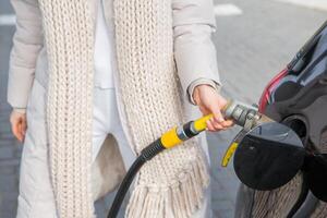 jong vrouw Holding een brandstof mondstuk in haar hand- terwijl tanken auto Bij gas- station. een hou op voor tanken Bij de gas- station. tanken de auto met gas. foto