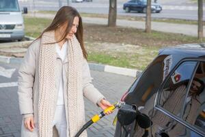 jong vrouw Holding een brandstof mondstuk in haar hand- terwijl tanken auto Bij gas- station. een hou op voor tanken Bij de gas- station. tanken de auto met gas. foto