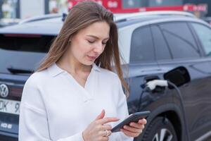 jong vrouw gebruik makend van een smartphone naar betalen voor elektrisch auto Bij de opladen station. opladen accu van opladen station. foto