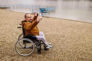 verlamd gehandicapten Mens in rolstoel is nemen selfie met smartphone buitenshuis. foto