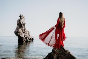 vrouw reizen zee. jong gelukkig vrouw in een lang rood jurk poseren Aan een strand in de buurt de zee Aan achtergrond van vulkanisch rotsen, Leuk vinden in IJsland, sharing reizen avontuur reis foto